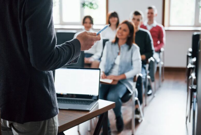 Un formateur, de dos, s'adresse à un groupe de professionnels assis qui l'écoutent.